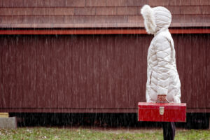 Person in a white winter coat holding a red toolbox while standing in the rain.