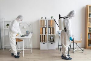 Cleaning professionals in protective suits are disinfecting an office space.