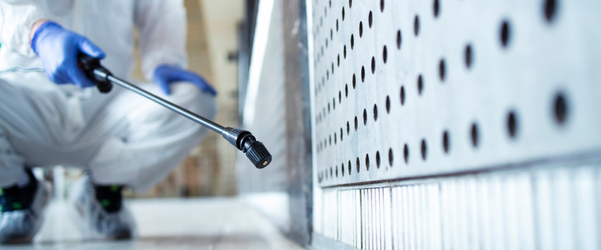 A pest control worker in a protective suit is spraying pesticide indoors for effective pest prevention.