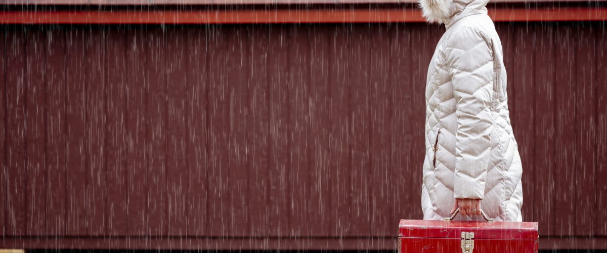 Person in a white winter coat holding a red toolbox while standing in the rain.